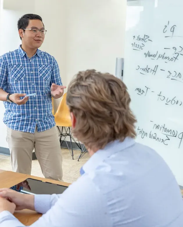 Two U N E students review the "4 P's" on a whiteboard